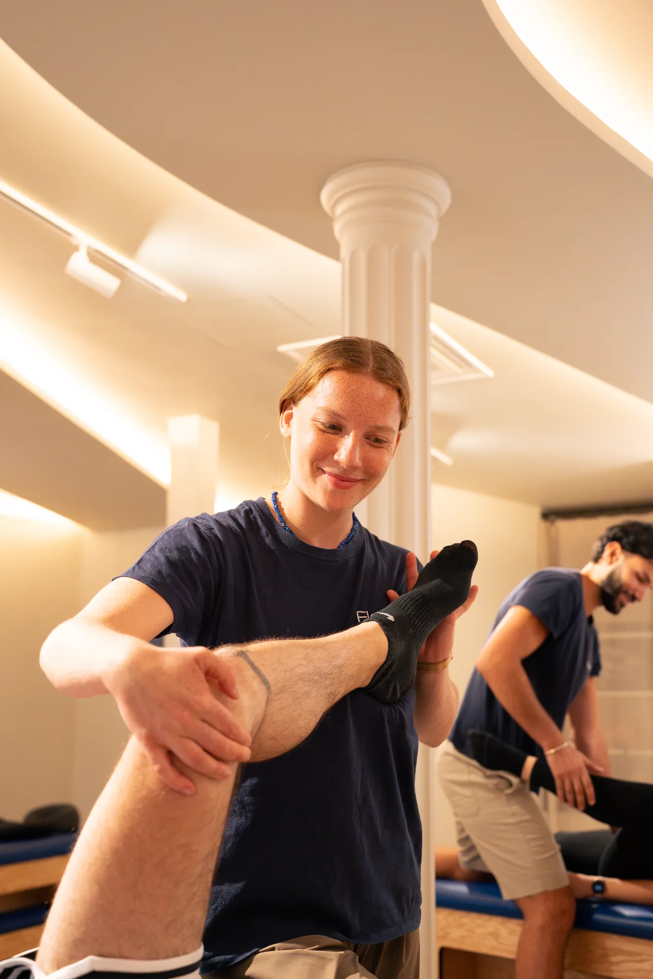 Une flexologue Flexlab étire la jambe d'un membre, devant les colonnes du studio du Sentier