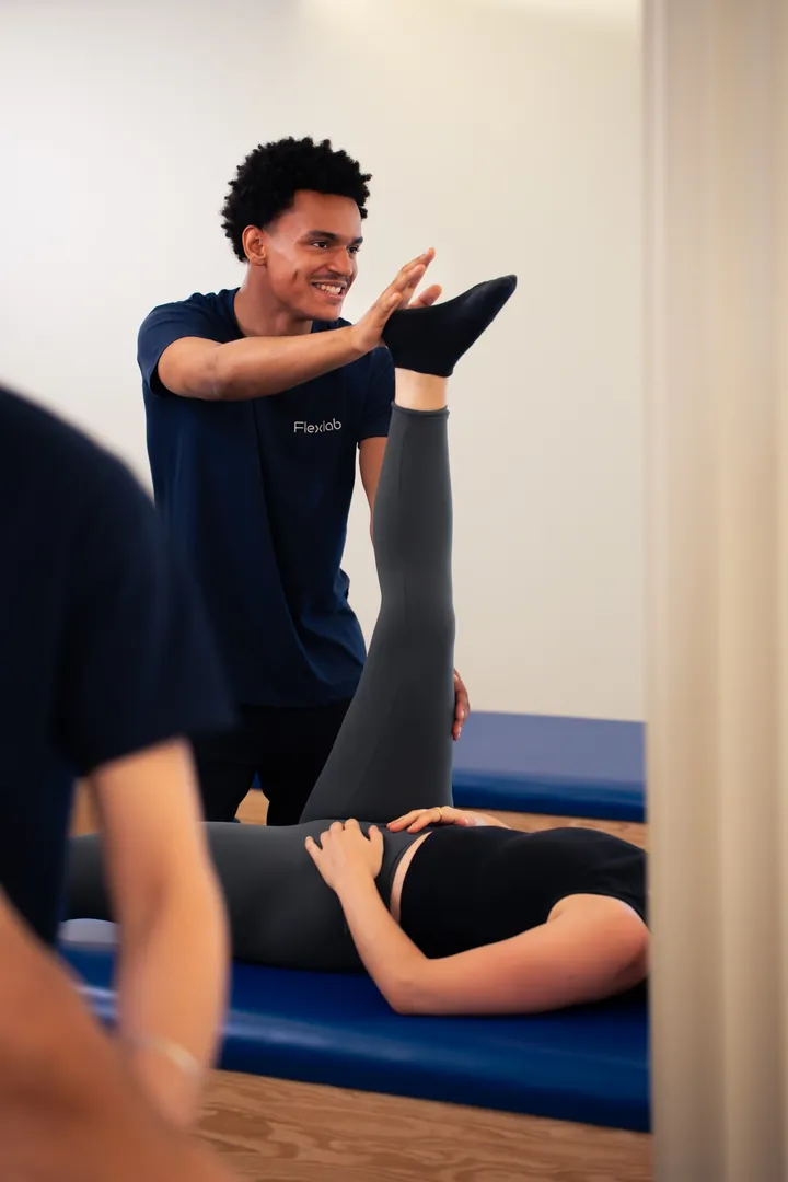 Le flexologue ouvre la hanche d’une cliente allongée, jambe tendue vers le haut.