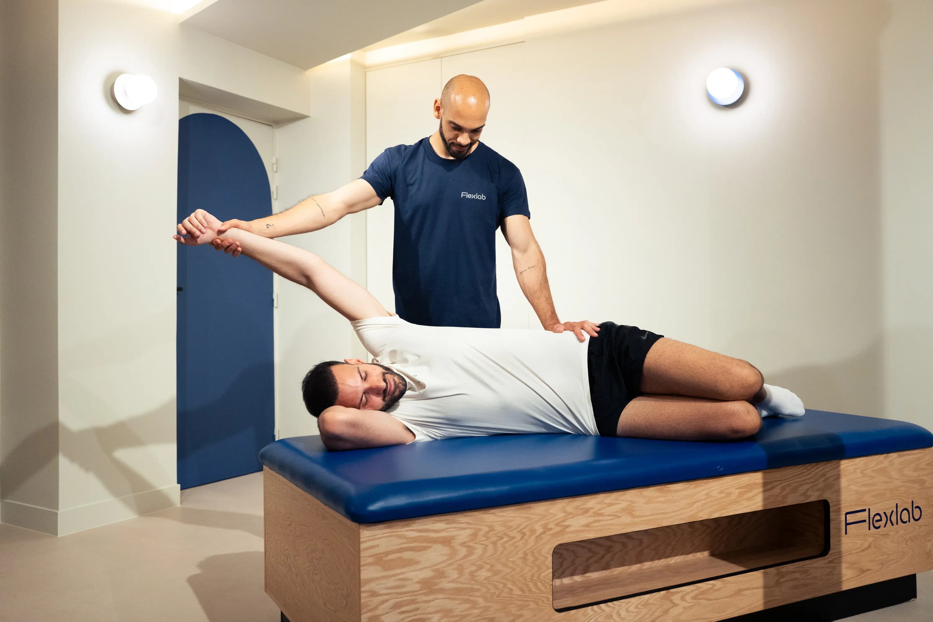 Le flexologue ouvre l’épaule d’un client allongé, bras tendu au-dessus de la tête.