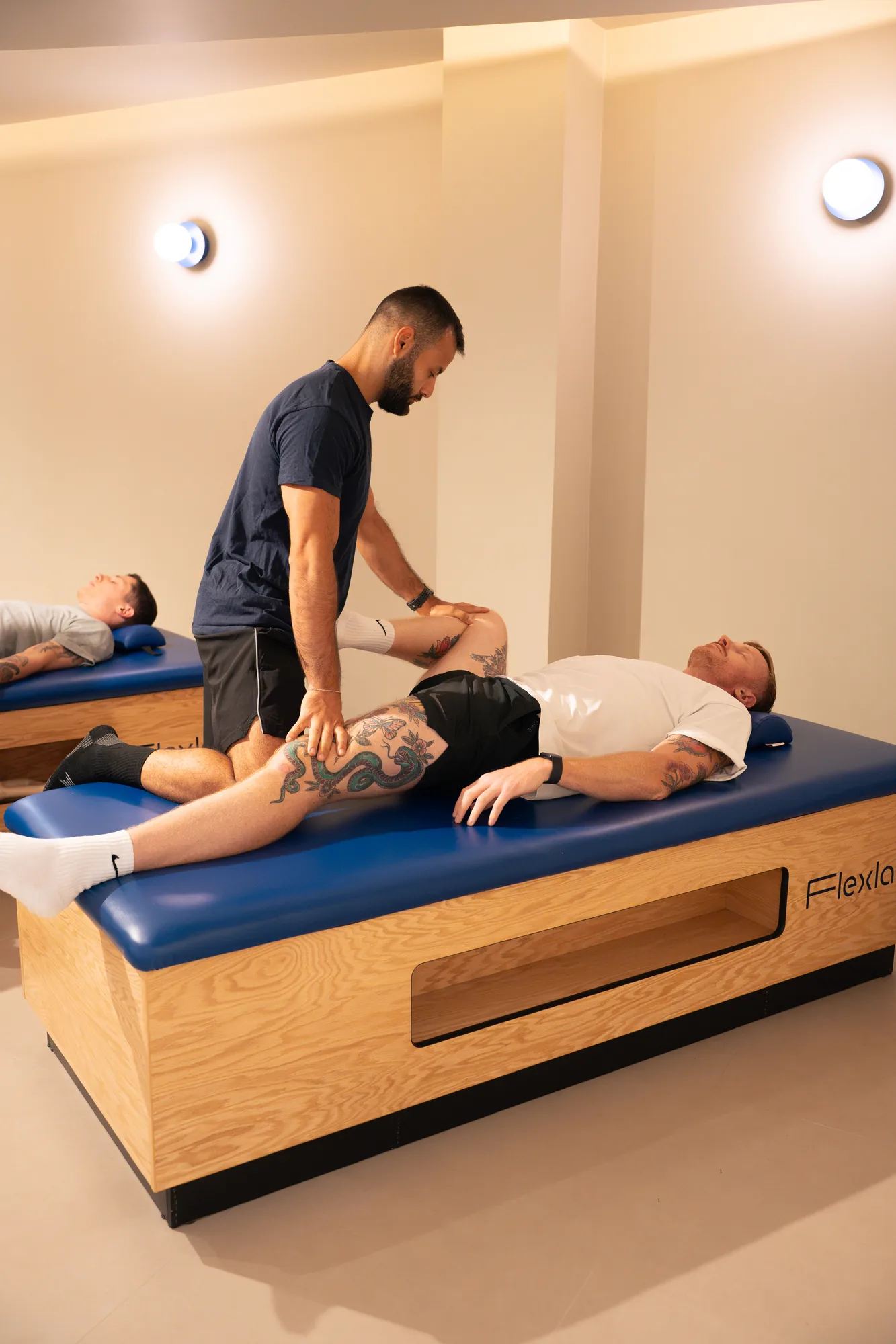 Un flexologue penché sur la table du studio, les mains sur la jambe d'un client allongé