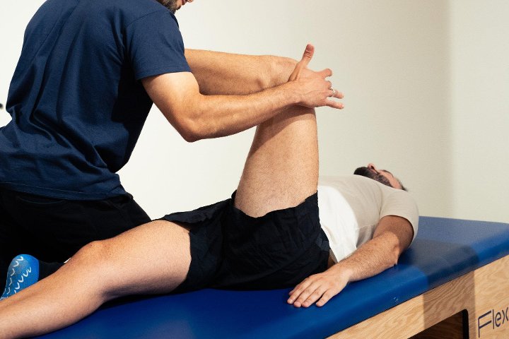 Un flexologue ramène la jambe d'un client vers la poitrine, sur la table